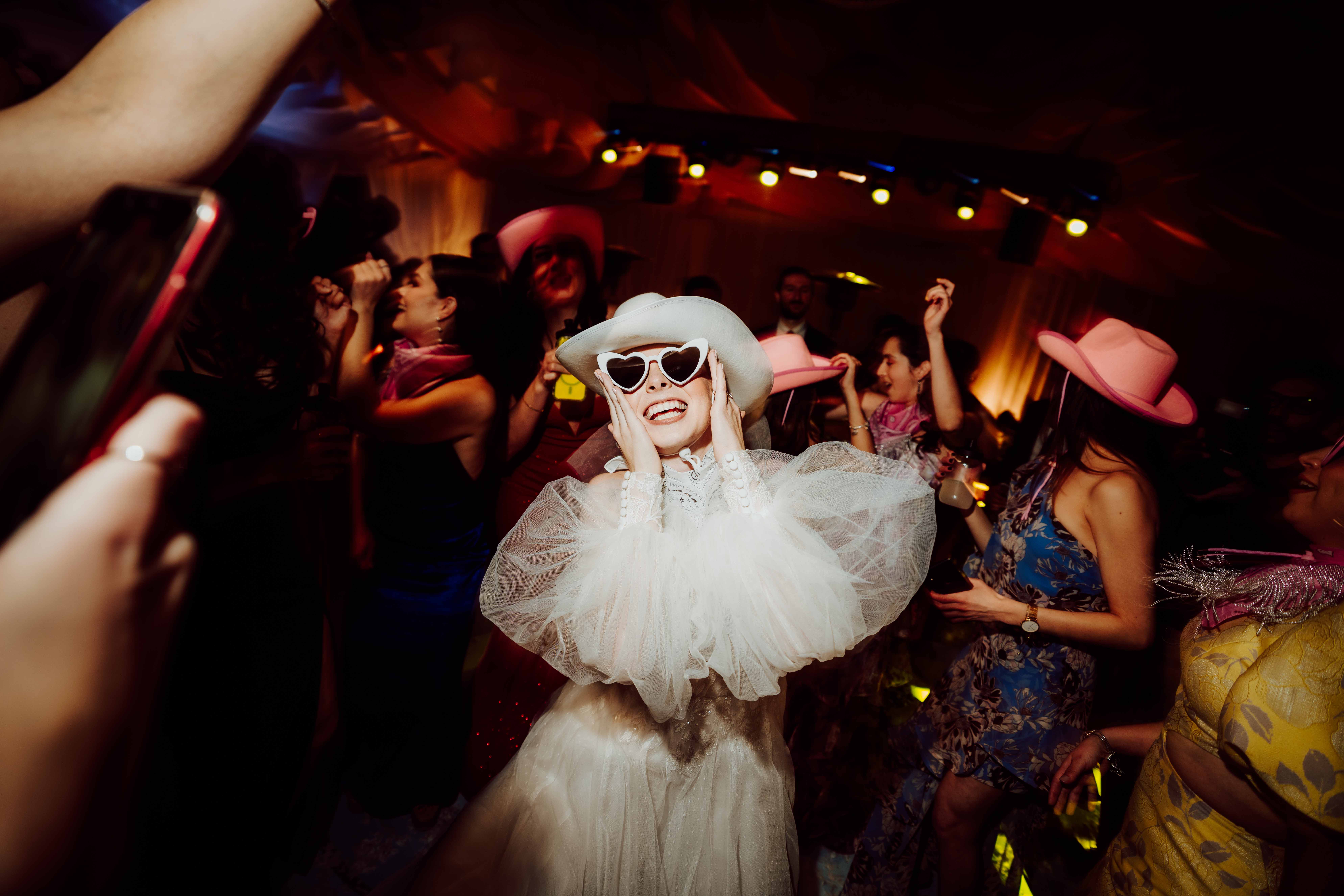 Novia con sombrero y lentes de corazón durante la fiesta de boda