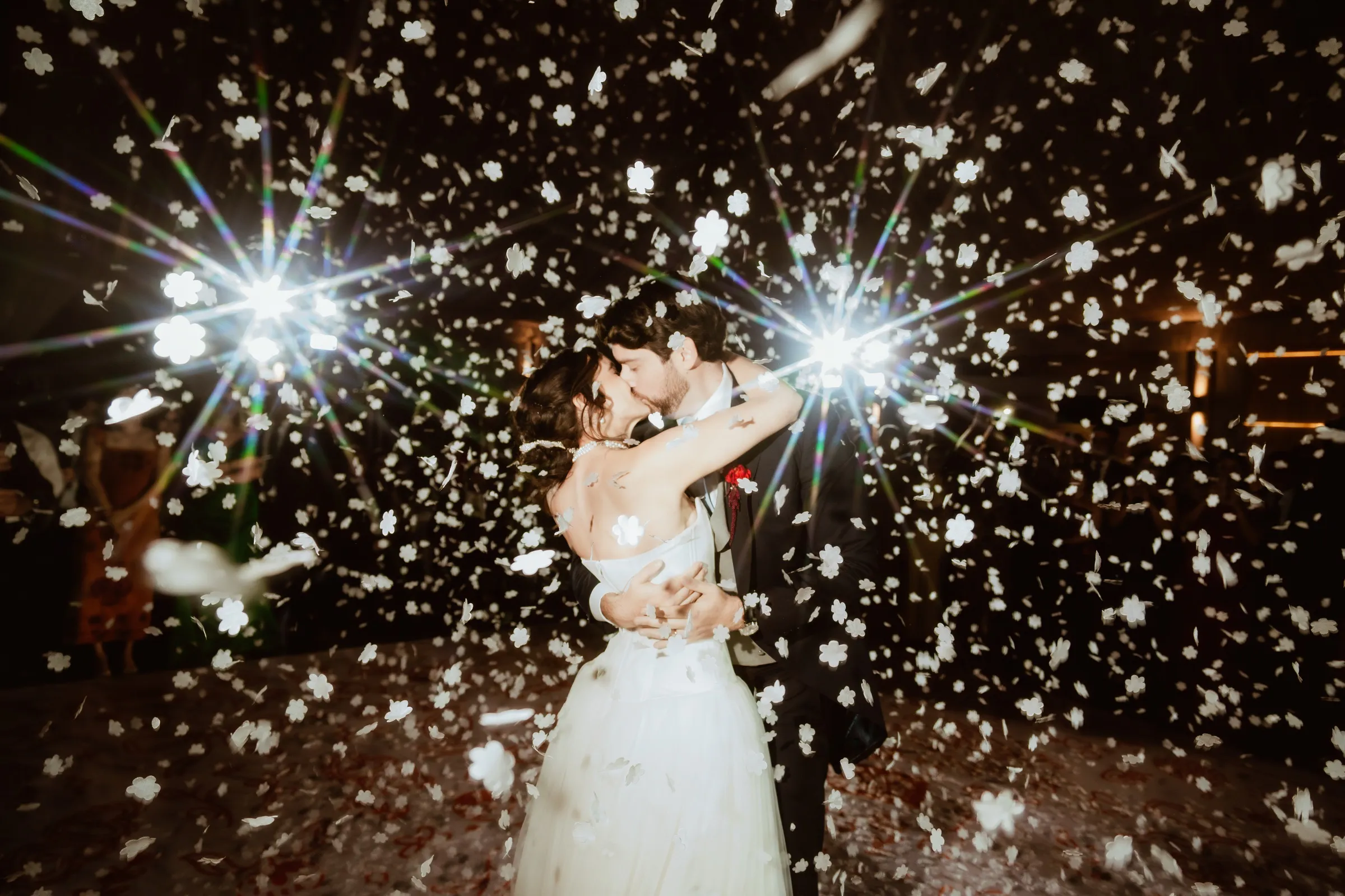 Beso de los novios entre confeti y luces durante la fiesta de boda