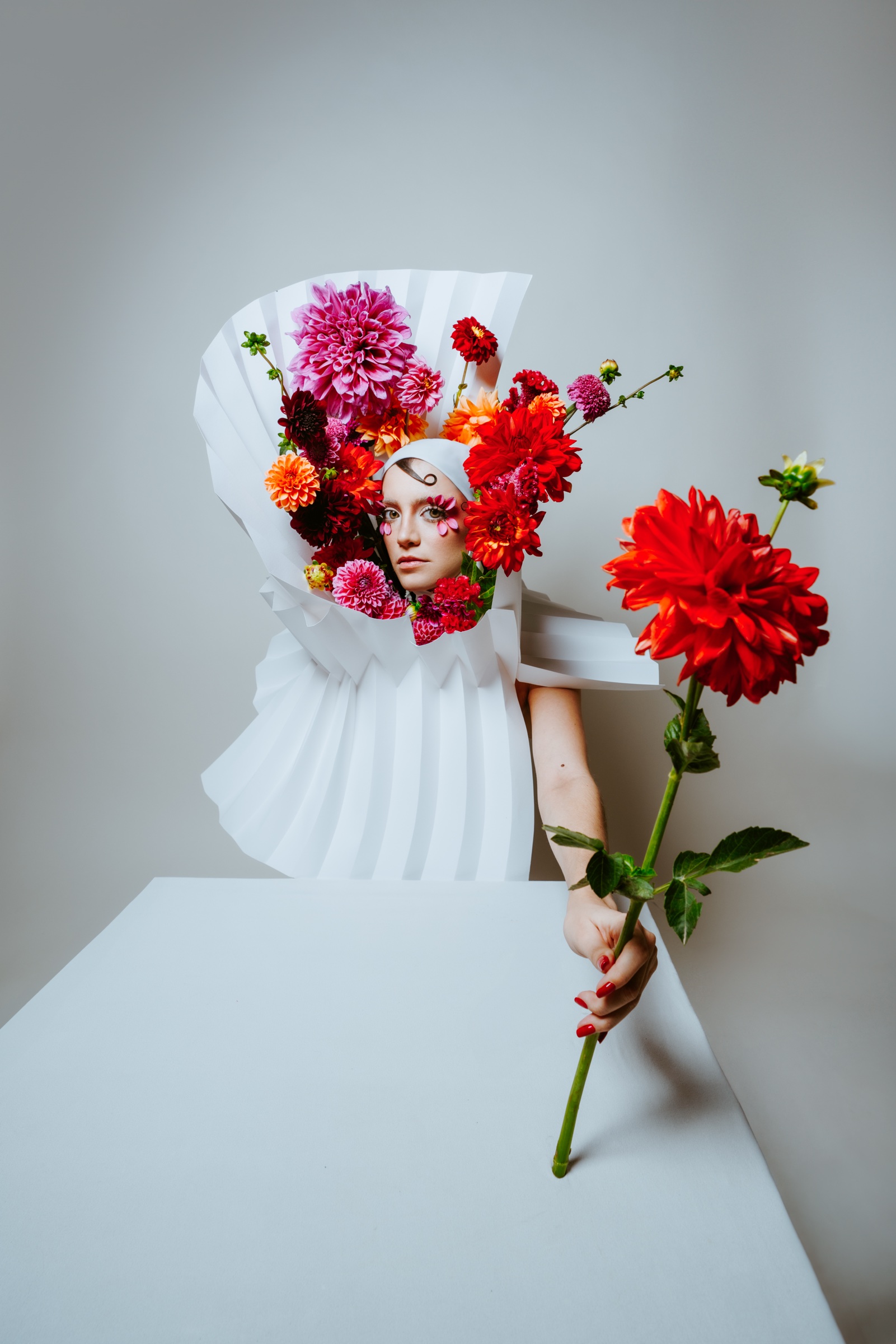 retrato editorial con flores de colores, papel blanco y una flor roja en la mano