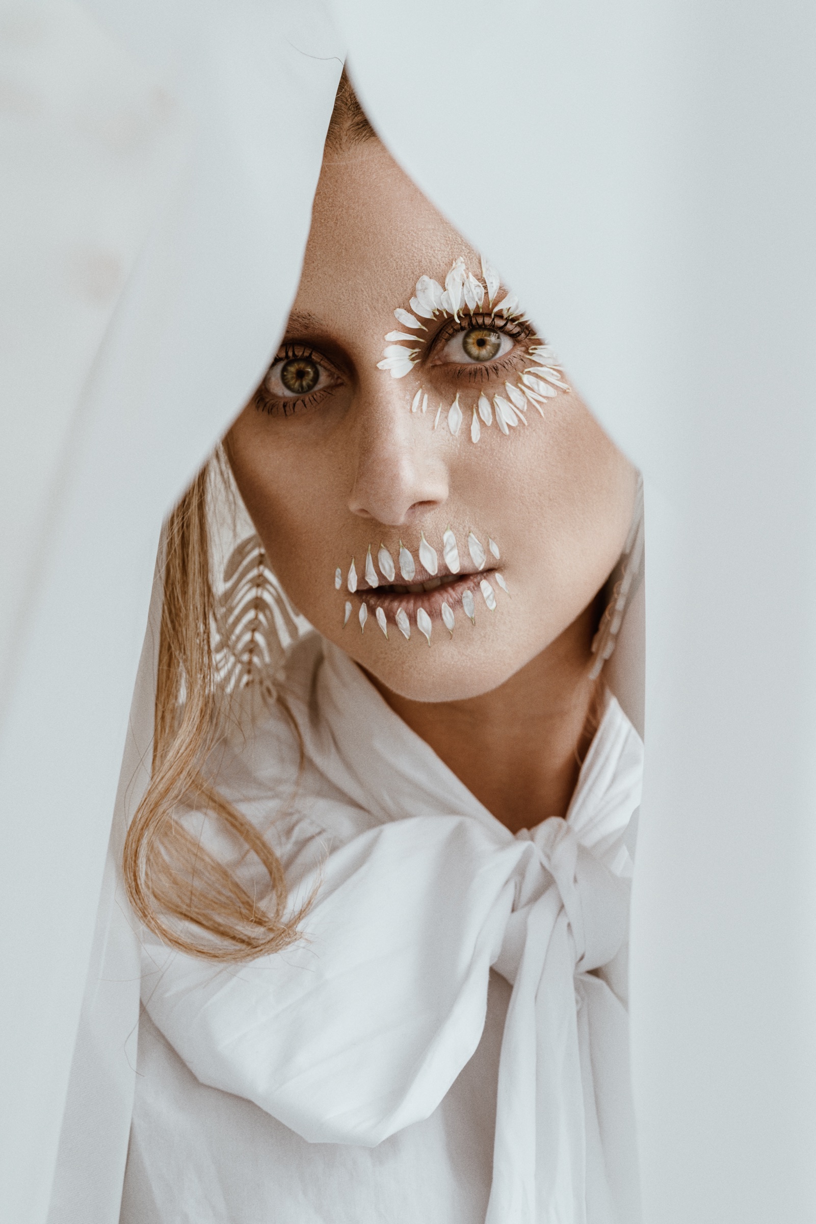 retrato editorial con pétalos blancos alrededor de los ojos y la boca