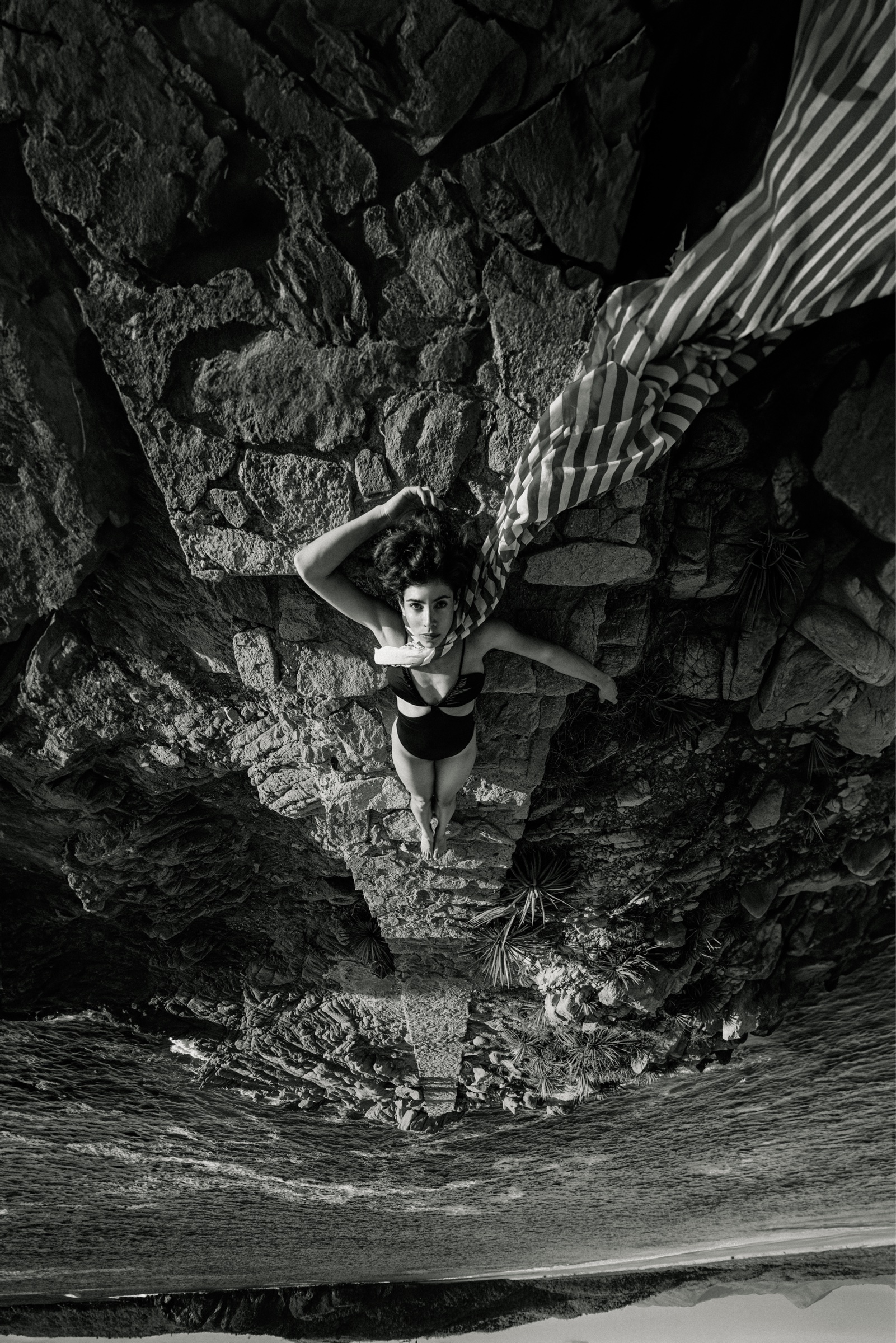 fotografía editorial en blanco y negro sobre rocas junto al mar con tela de rayas