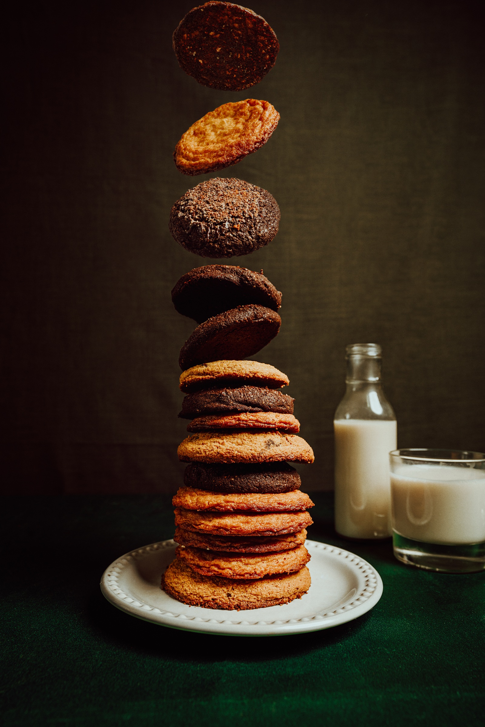 fotografía gastronómica de galletas apiladas junto a leche sobre fondo oscuro