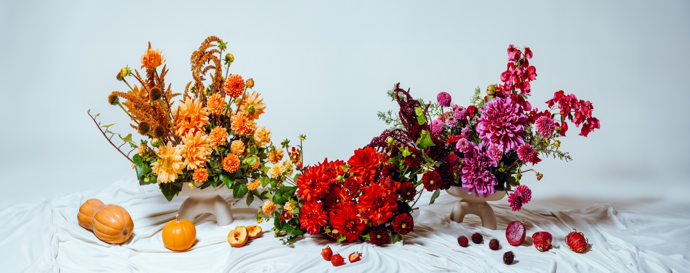 bodegón con arreglos florales de colores y frutas sobre tela blanca
