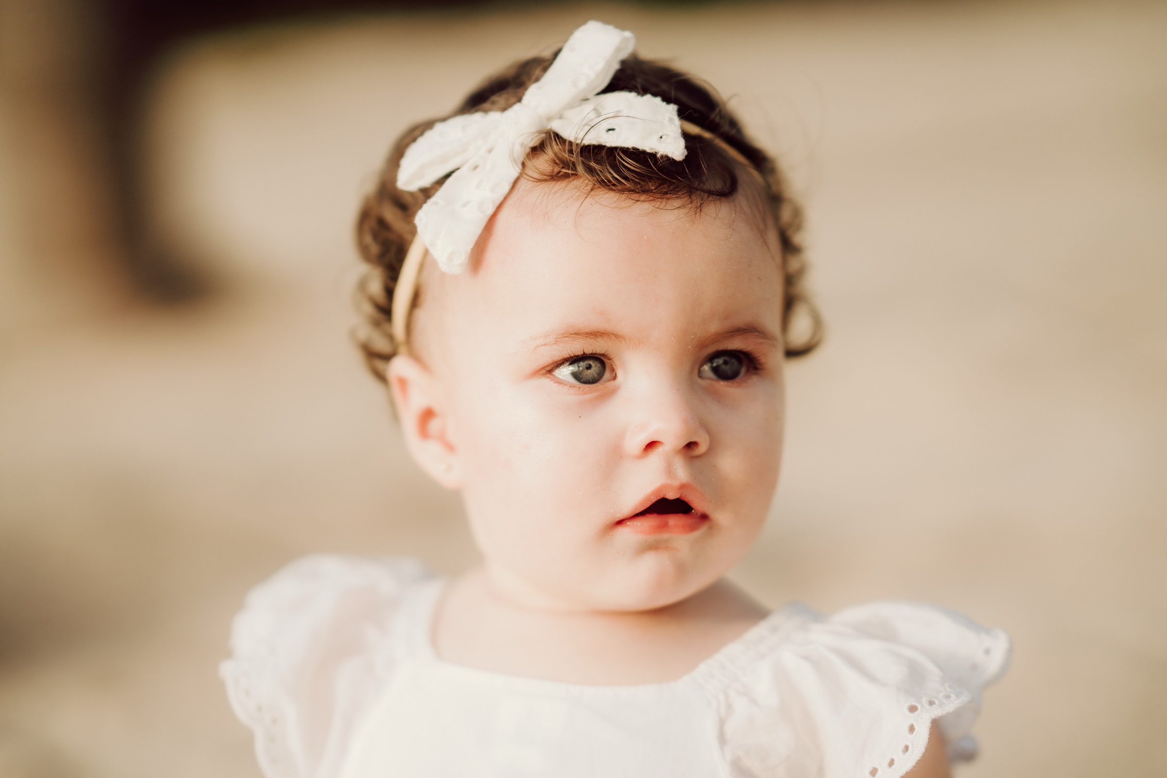 retrato infantil de un bebé con vestido blanco y un moño en el cabello