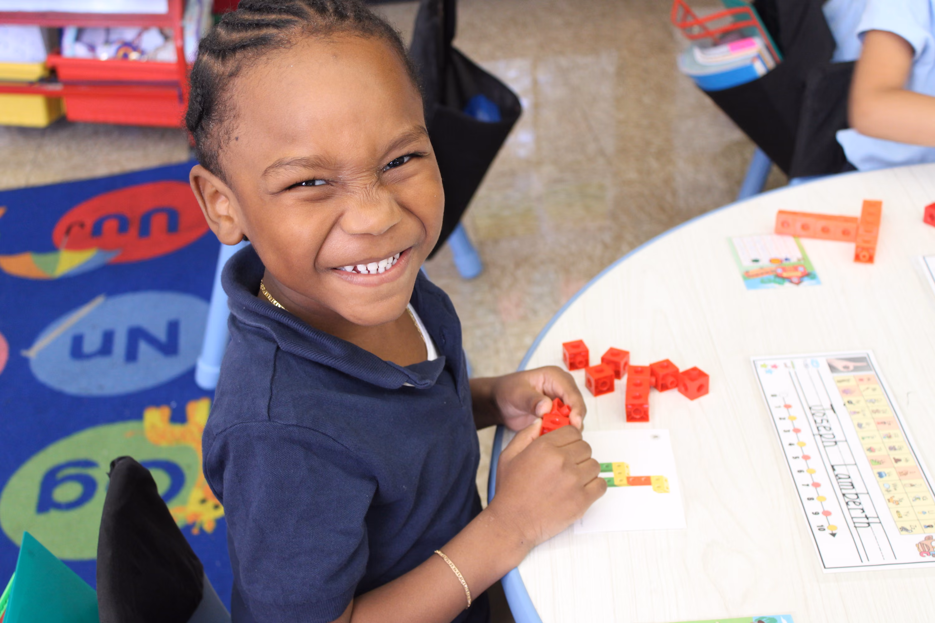 Smiling student building shapes with red connecting cubes