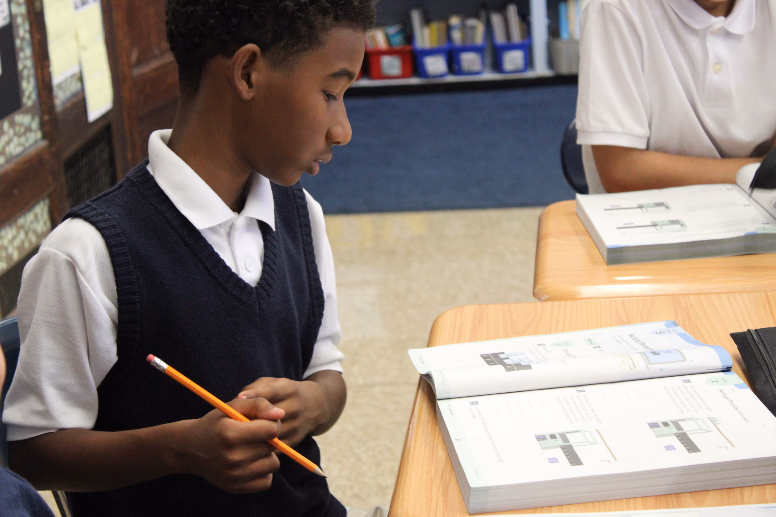Student in uniform holding pencil and reading open textbook