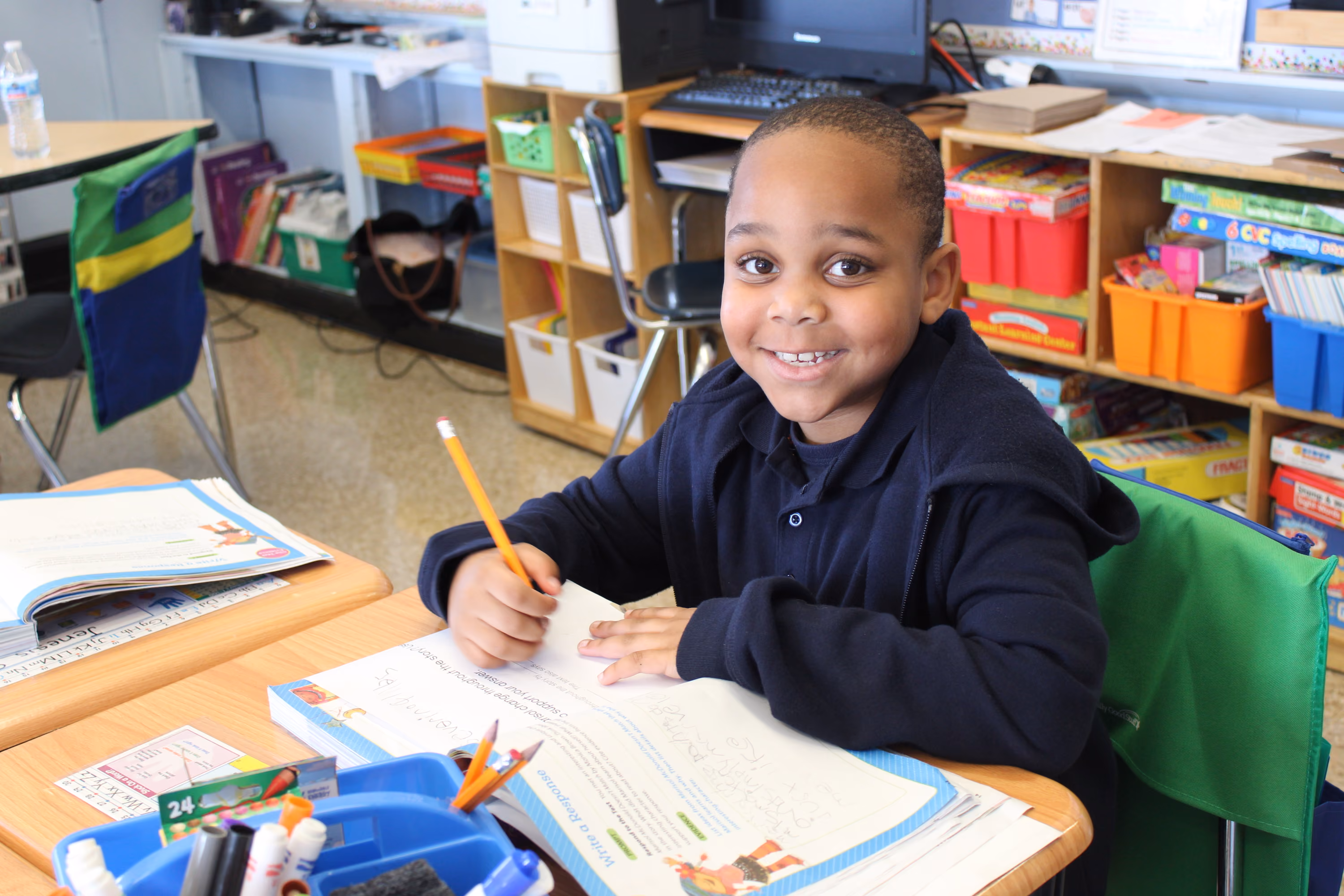 Smiling student writing in workbook at classroom desk