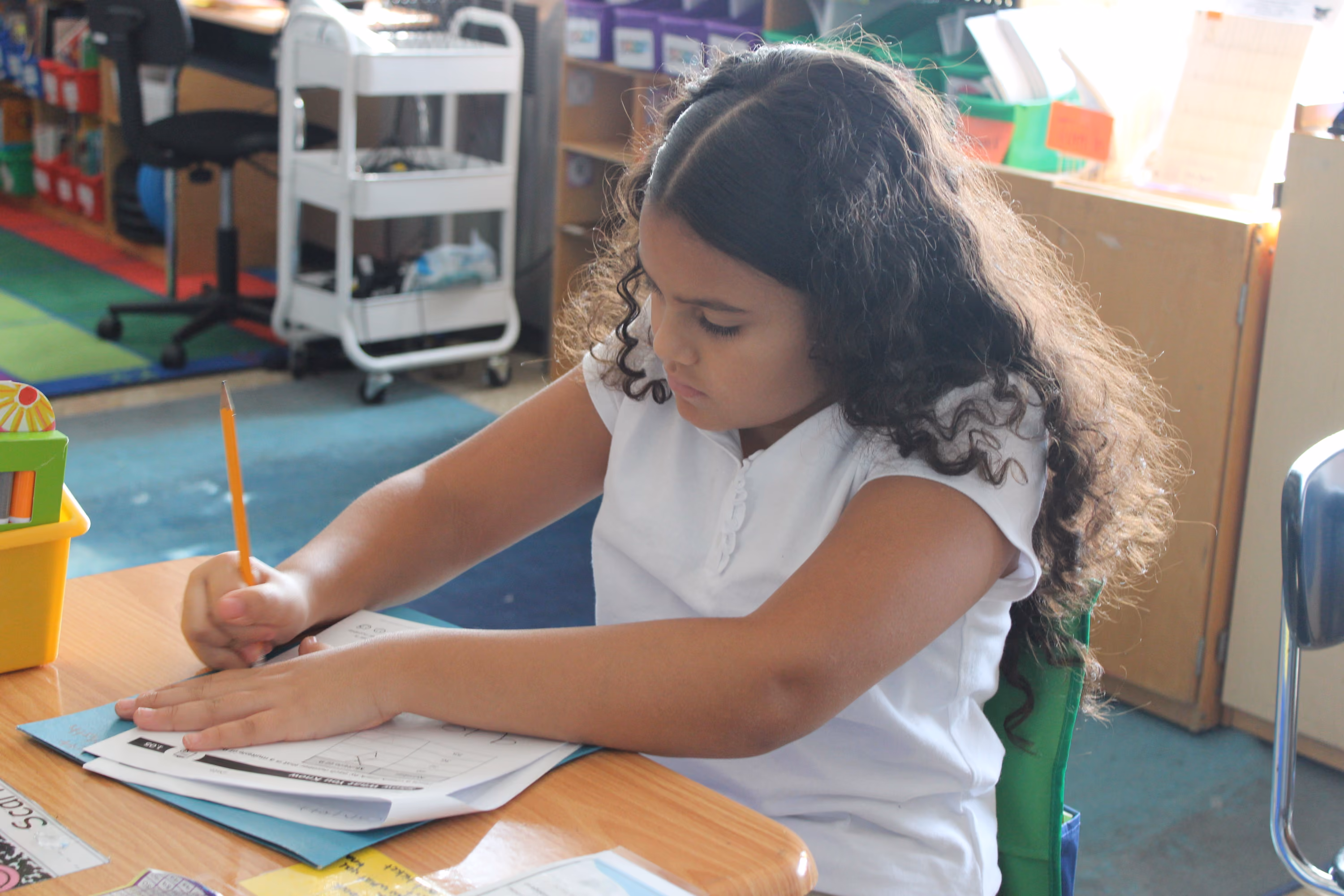 Student writing with pencil on worksheet at classroom desk