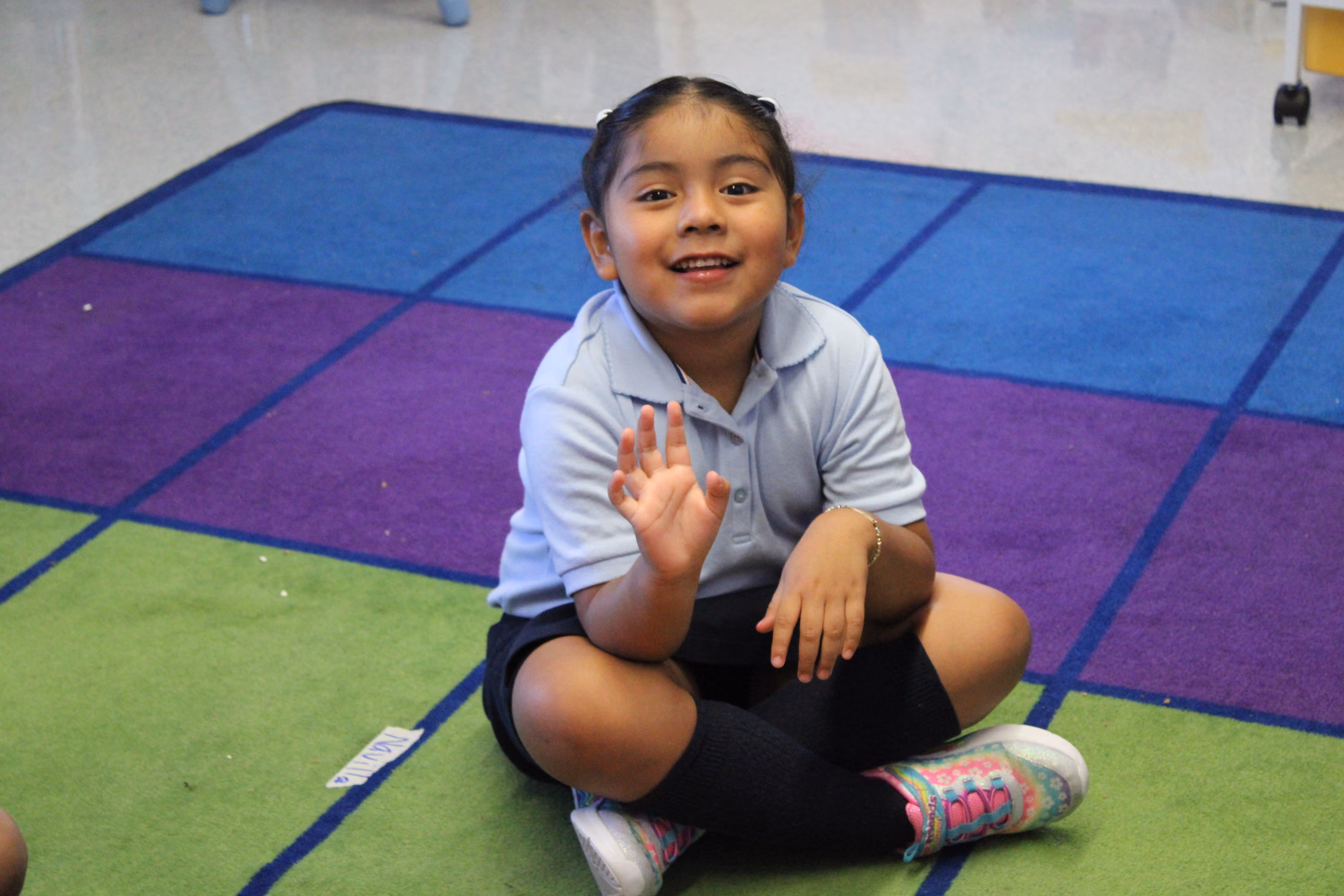 Smiling student in uniform sitting on colorful classroom rug