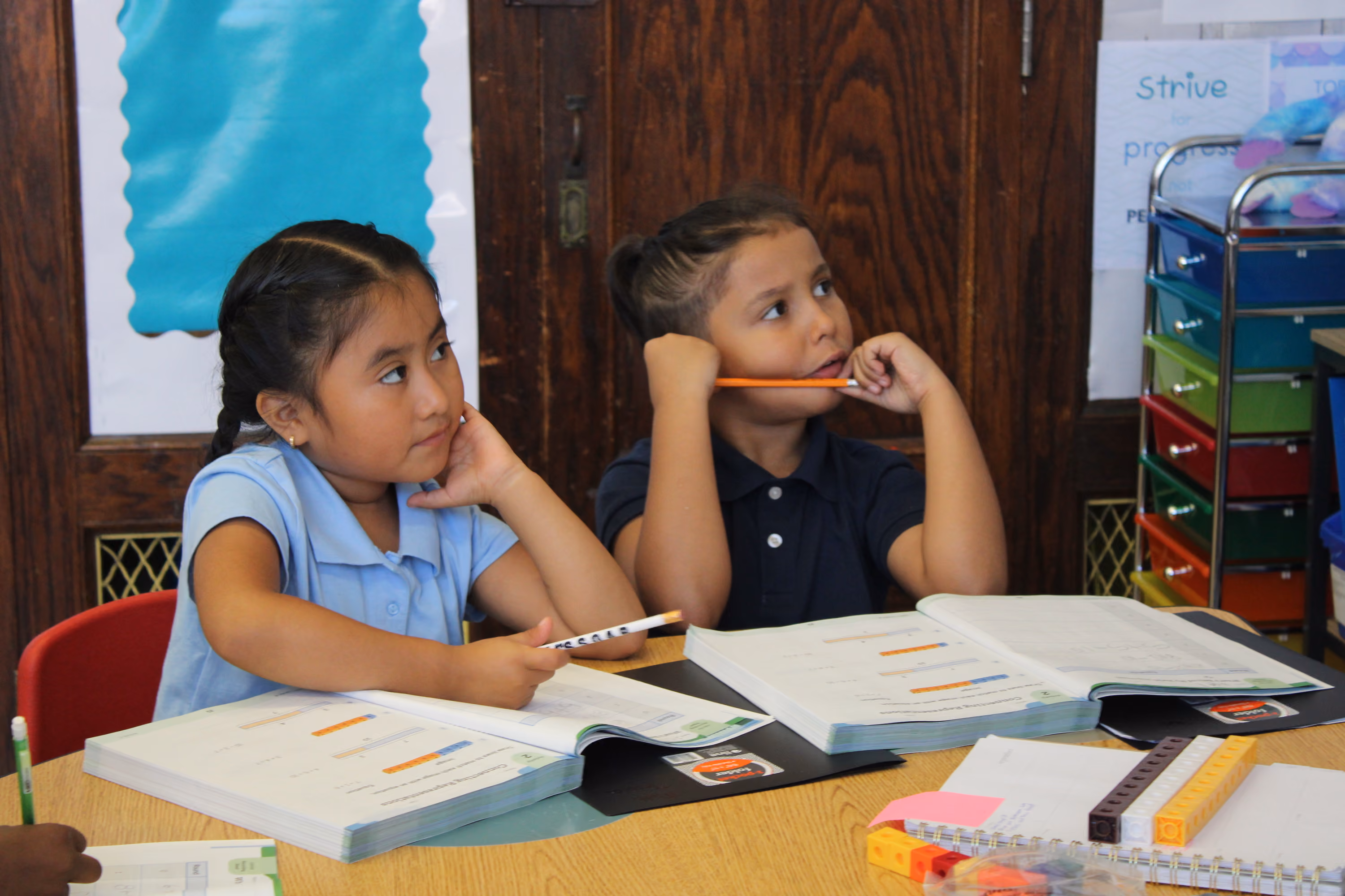 Two students listening attentively with pencils at classroom desk