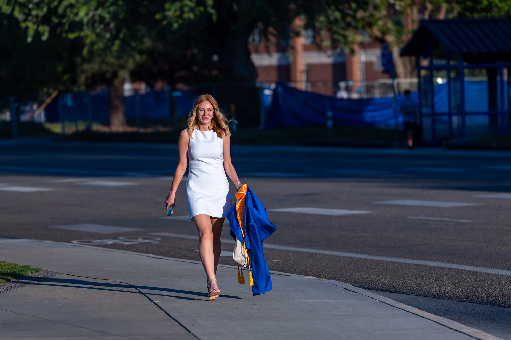 A Boise State graduate walking with her cap and gown.