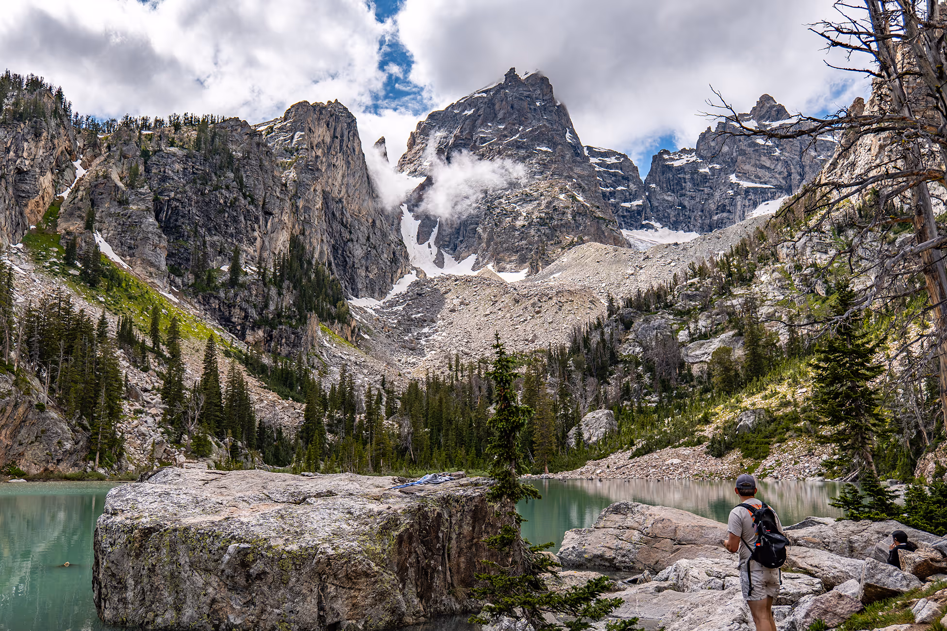 A hiker staring at the Tetons at Delta Lake during a cloudy day