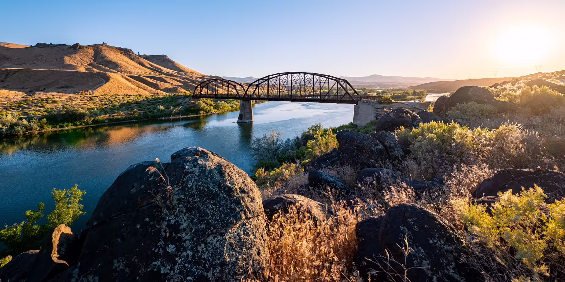 Sunset over river with foreground rocks and a bridge at Celebration Park, Idaho