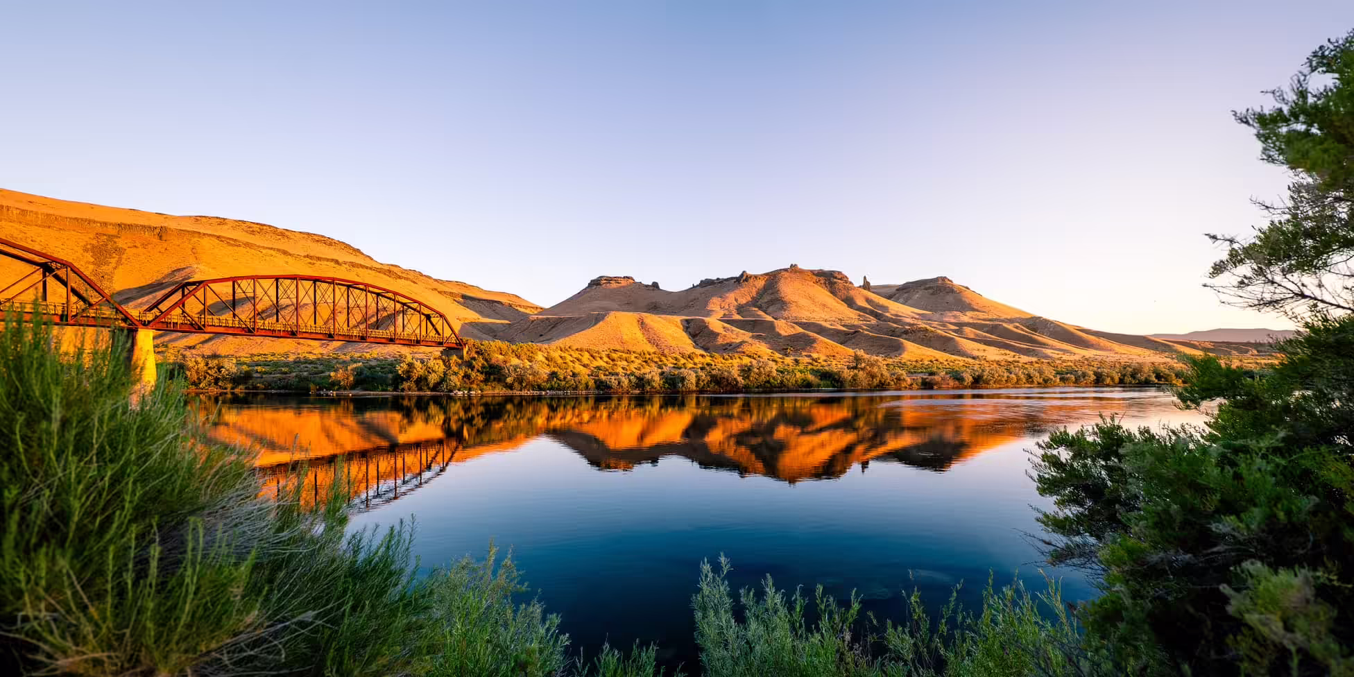Grass-framed landscape of Celebration Park, Idaho, at sunset, with foreground grasses and a colorful evening sky.
