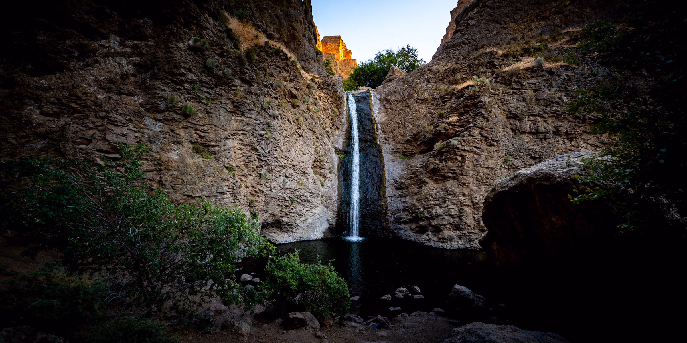 Cascading waterfall at Jump Creek Falls in Idaho, surrounded by rocky cliffs, boulders and dense trees in a rugged canyon