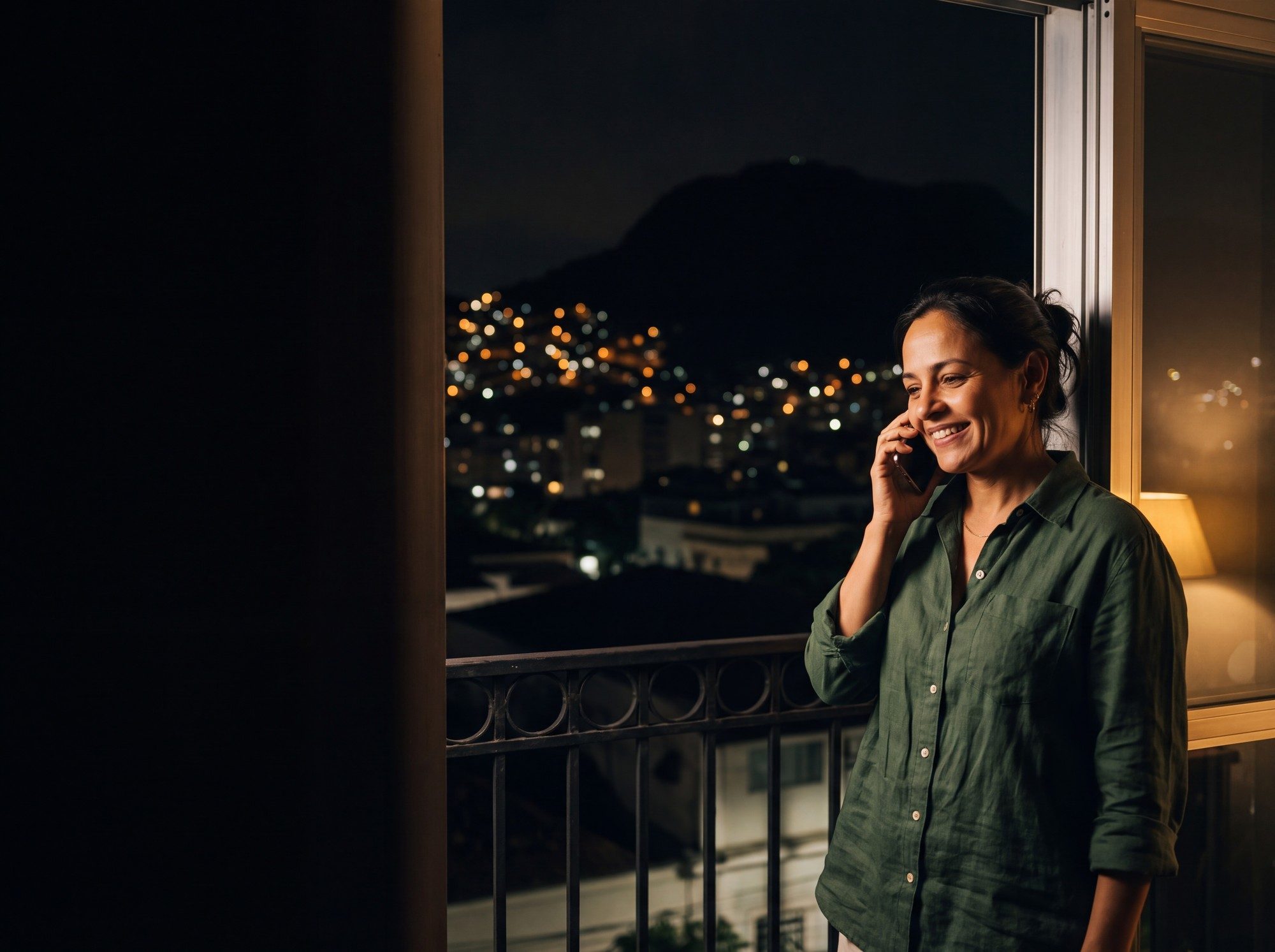 Carolina at home in Rio de Janeiro at night, phone to her ear, smiling
