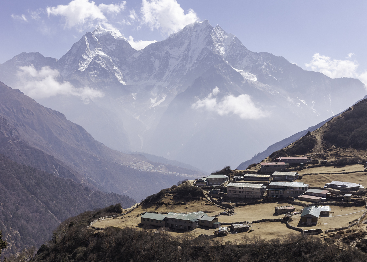 Mountain village with buildings on a hilltop under misty snow-covered peaks.