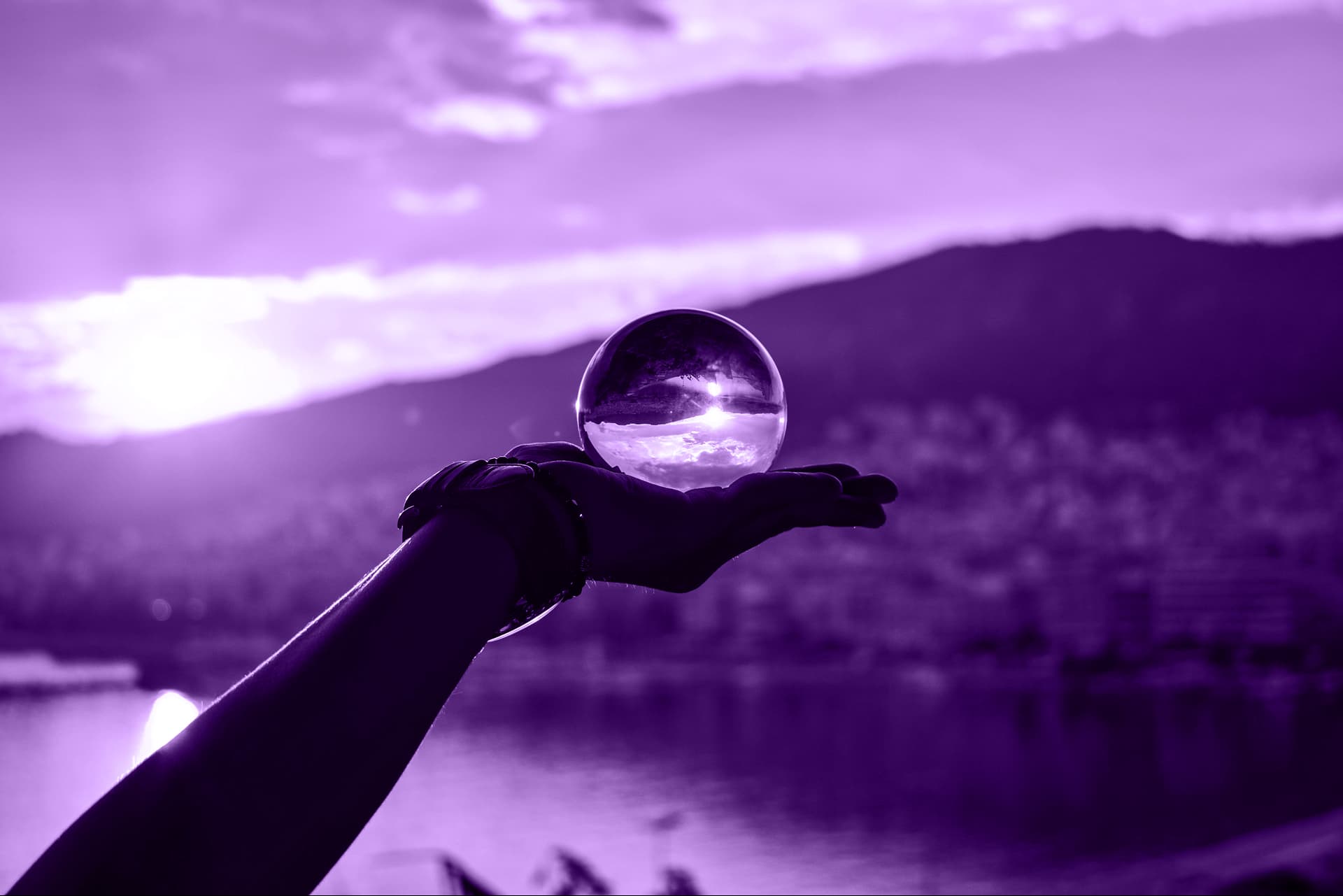 A hand infront of a landscape view holding a glass orb