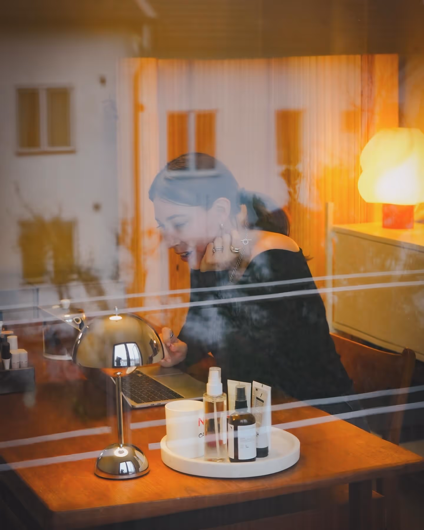 Lina Livian som grundande Glowaddictions sitter och arbetar vid en dator vid ett skrivbord i teak, i bakgrunden lyser en lampa, bilden är tagen i glowaddictions kontor och genom ett fönster