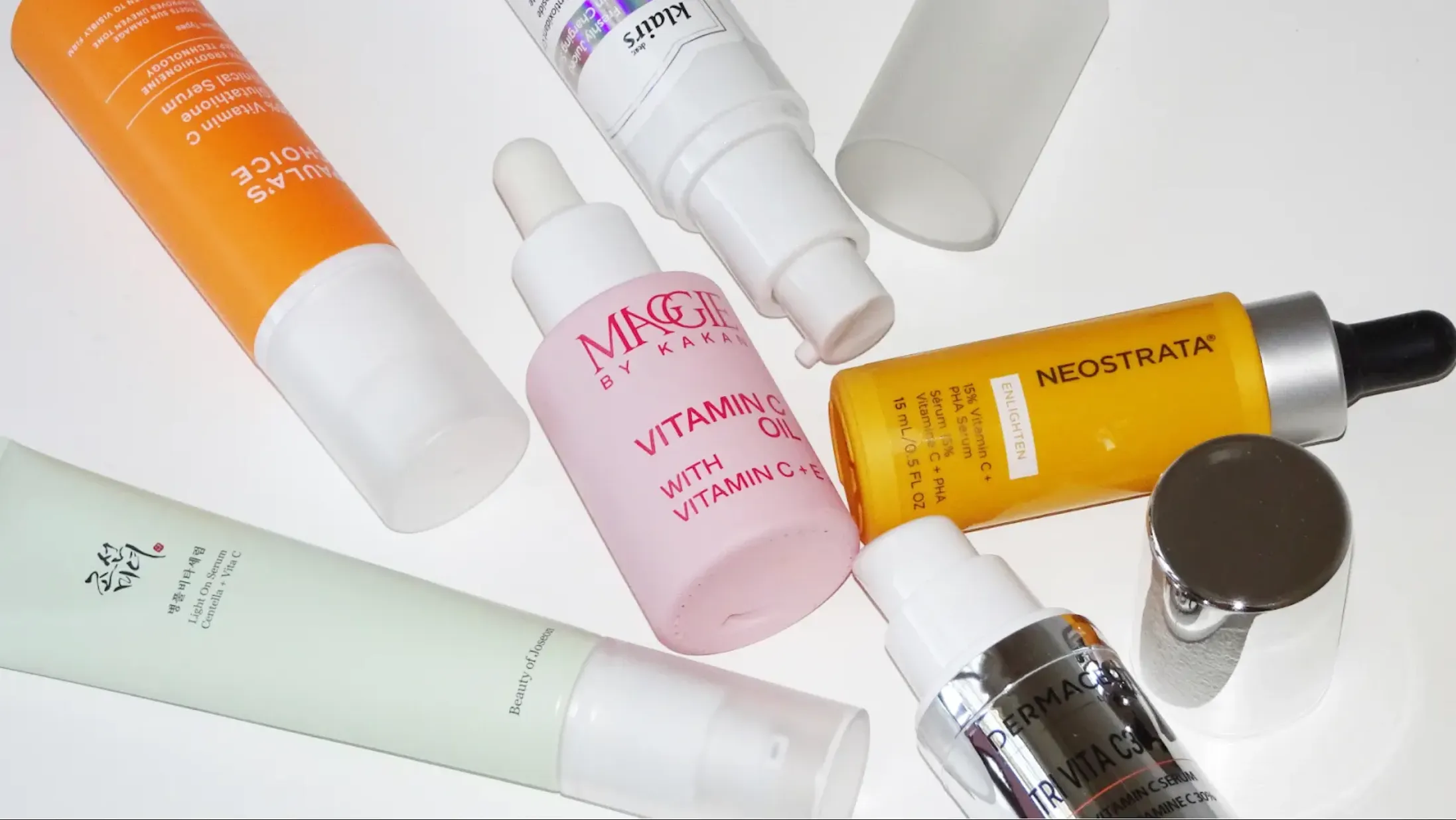 Flera olika C-vitaminserum från olika märken ligger utspridda på ett vitt underlag.