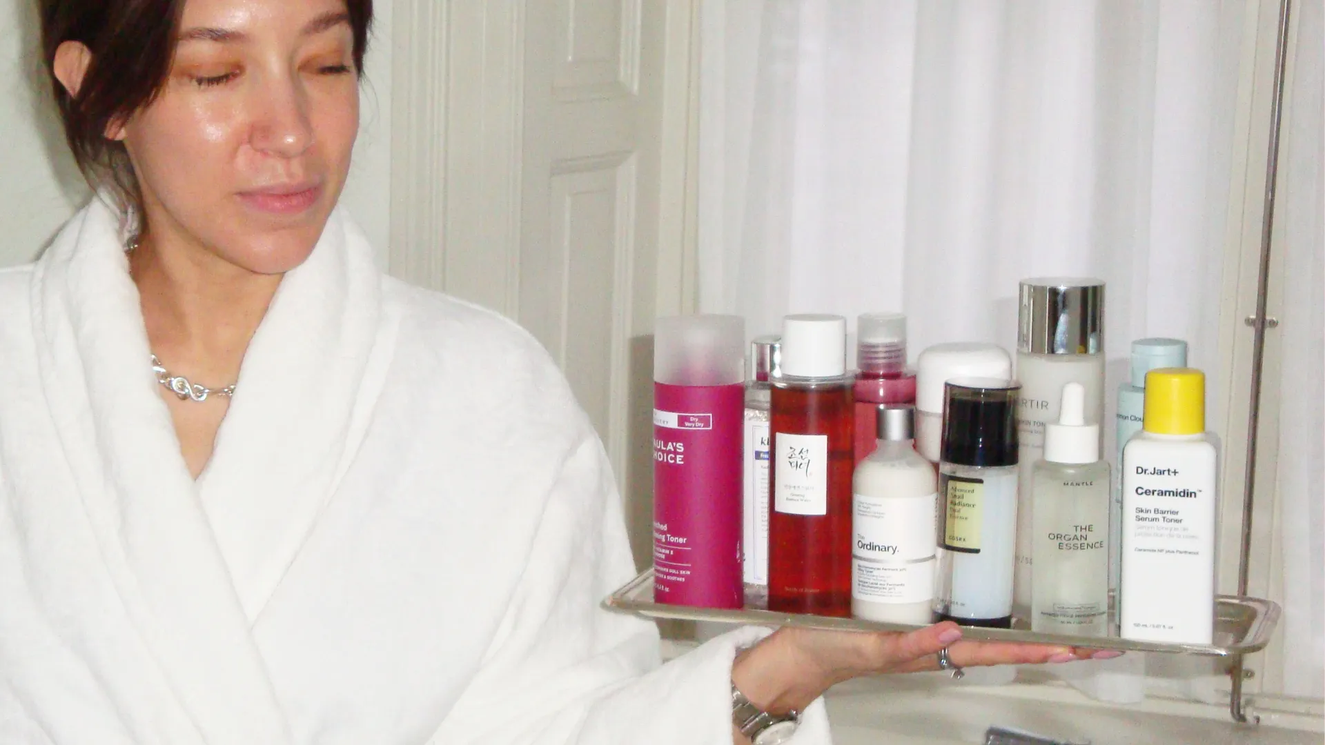 Lina Livian som grundade Glowaddictions har morgonrock och håller en bricka med Essence för hudvård i ett badrum, vi har testat essence.