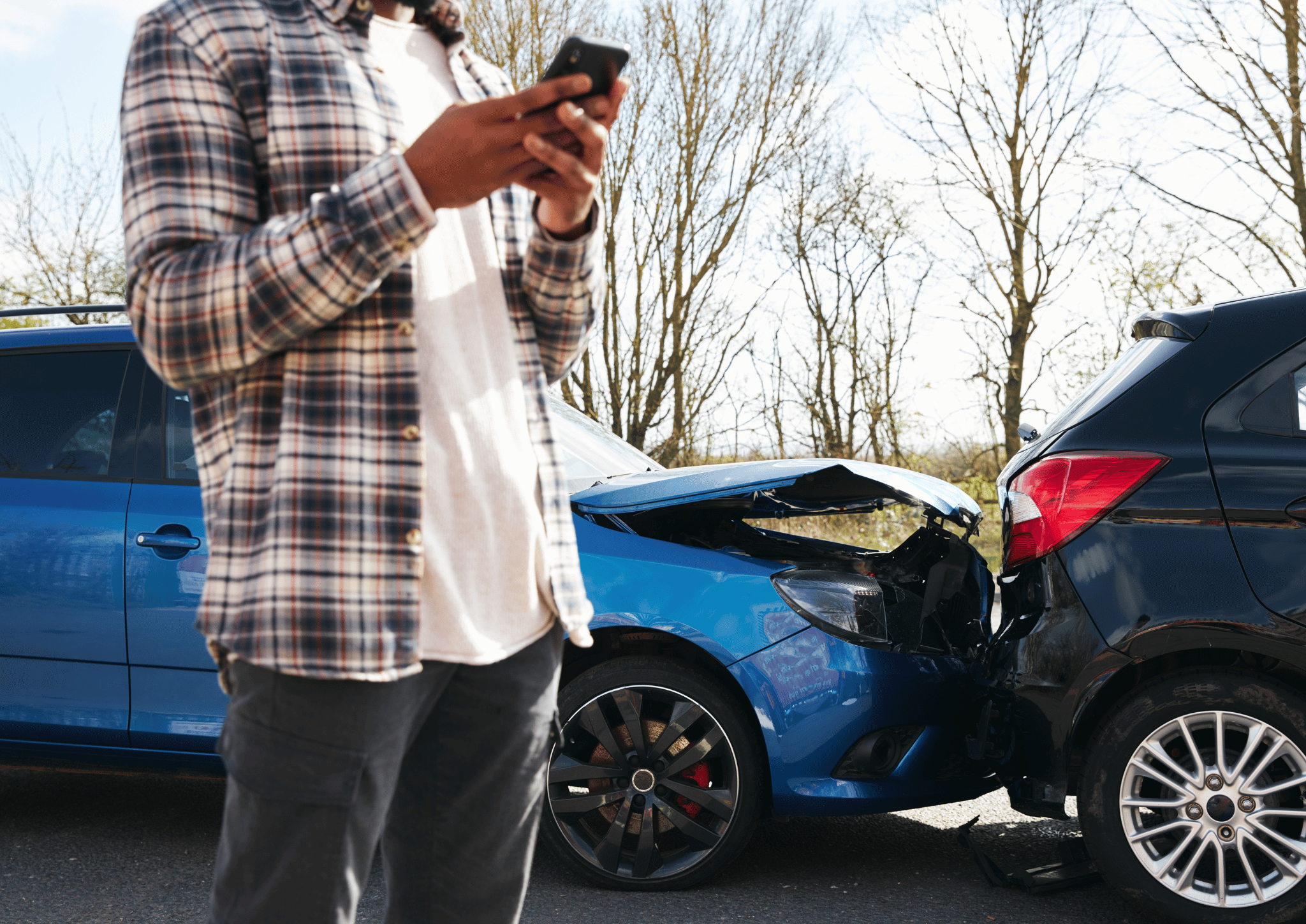 Ein Mann der zu seinem Handy greift nach einem Unfall. Im Hintergrund ein Auto was einem anderen angefahren ist.