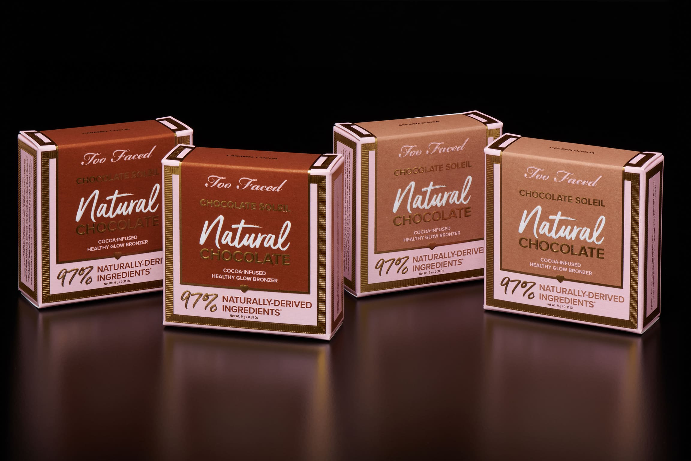 Four Too Faced Chocolate Soleil Natural Chocolate bronzer boxes in two shades, Caramel Cocoa and Golden Cocoa, on a dark reflective background.