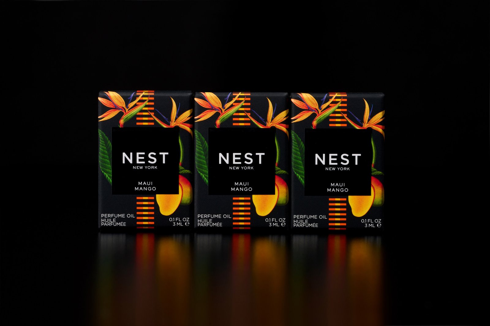 Three NEST New York Maui Mango perfume oil boxes in black tropical floral packaging with bird-of-paradise flowers and mango illustration, displayed against a black reflective background