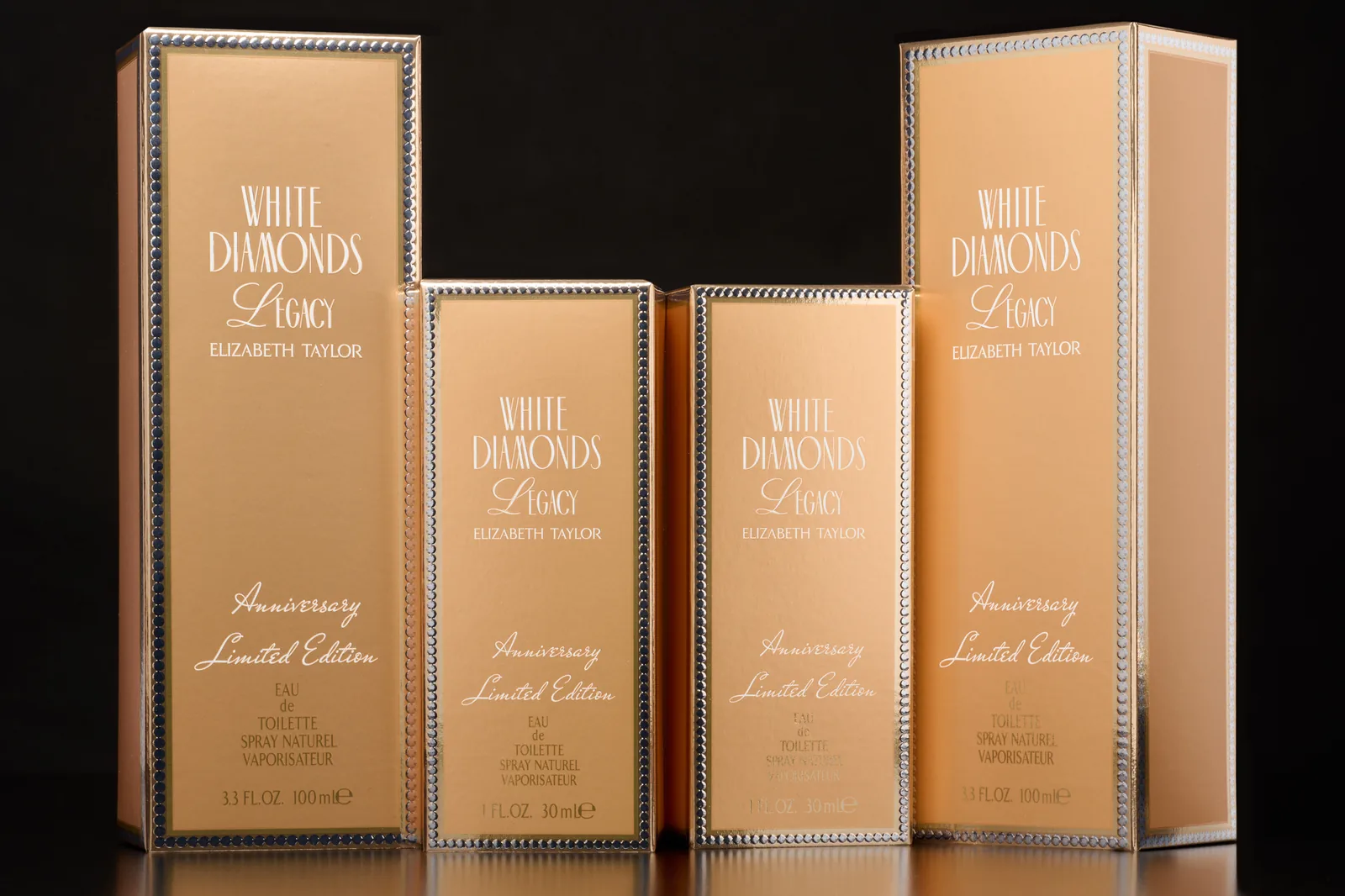 Four White Diamonds Legacy by Elizabeth Taylor perfume cartons in gold with pearl-bead borders, in 30 ml and 100 ml sizes, against a black background