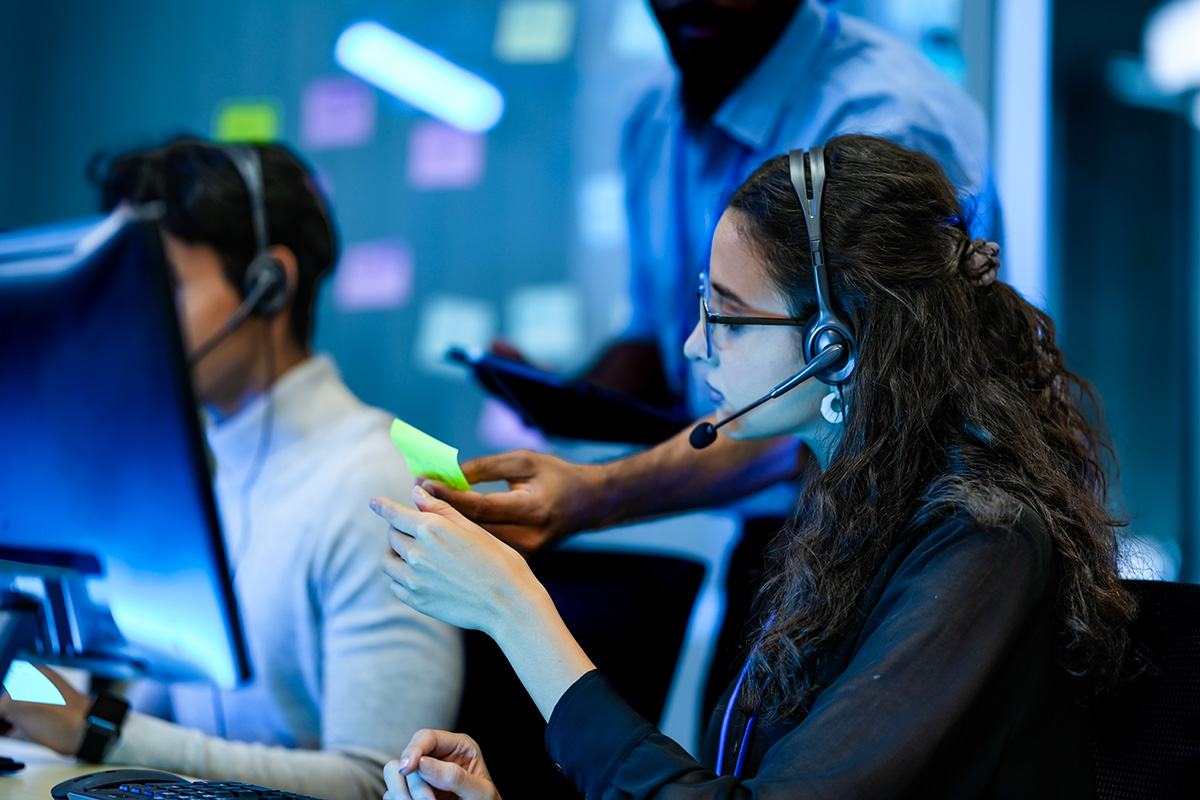 IT help desk cost-per-ticket benchmark data displayed on screens as agents collaborate at workstations in a modern support center