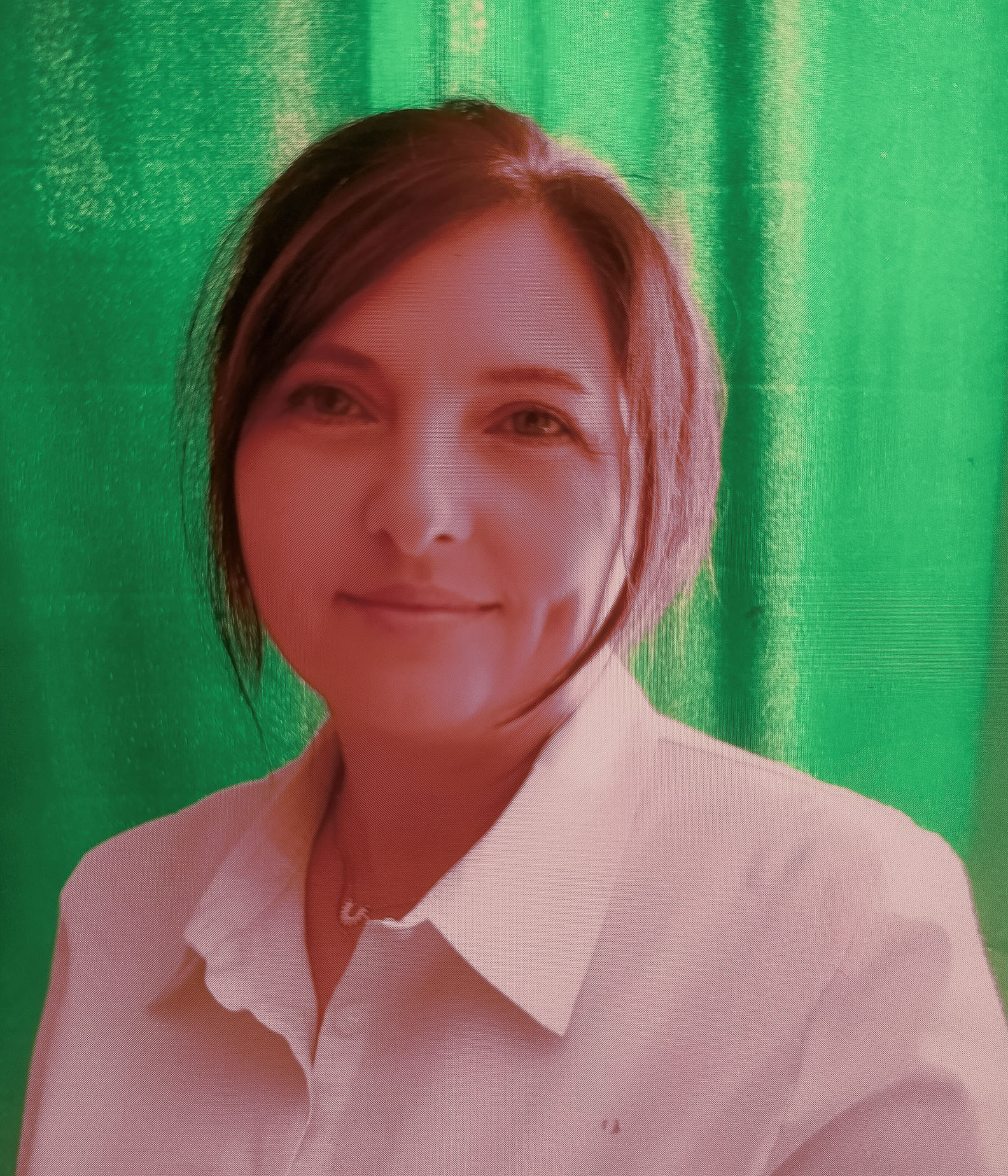 Portret kobiety w białej bluzce na tle zielonej zasłony, patrzącej przyjaźnie w obiektyw.