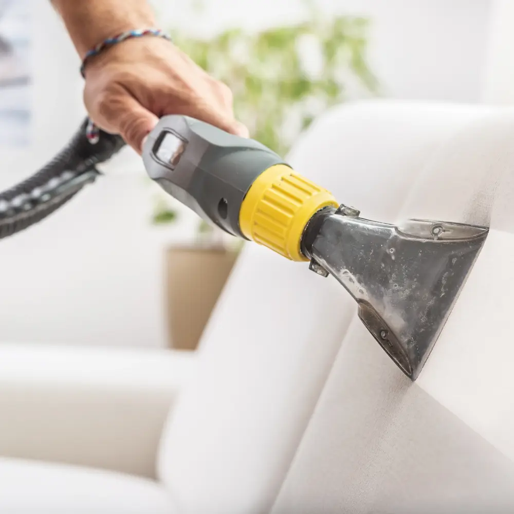 A close-up of a person using a vacuum extractor on a white sofa, symbolizing deep cleaning services for thorough home care.