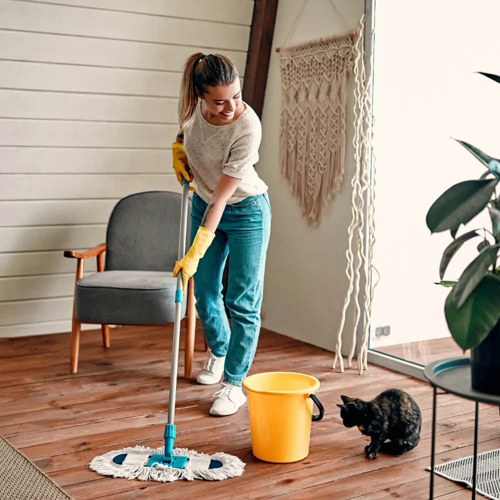 A woman mopping a hardwood floor in a cozy living room, representing standard house cleaning services with attention to detail.