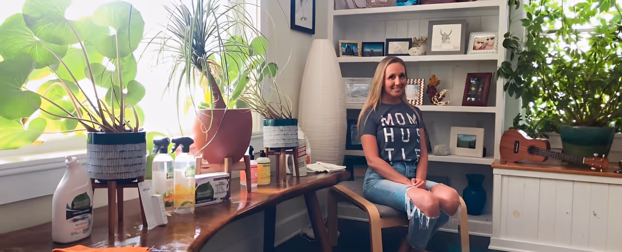 Emily, founder of Holistic Cleaning Company, sitting in her home workspace surrounded by natural cleaning products and plants, representing her health-first approach to eco-friendly cleaning.