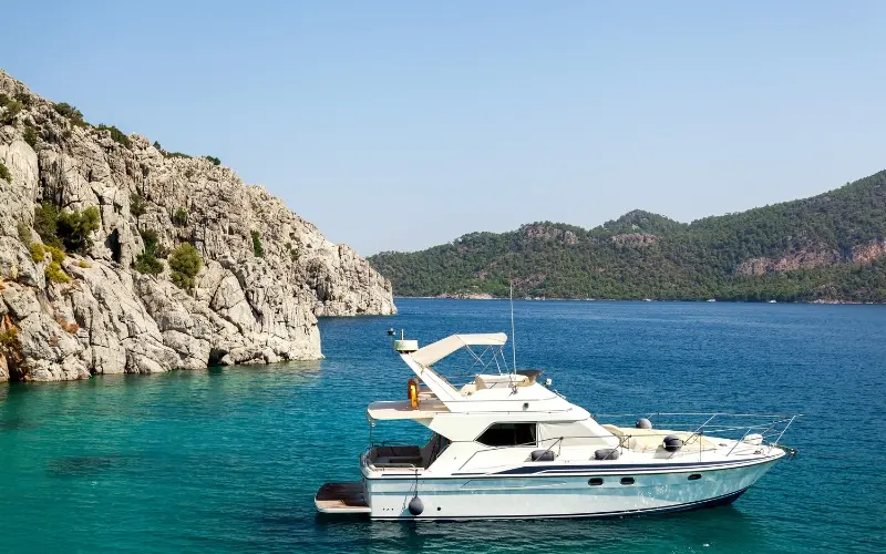 Motor yacht anchored near rocky coastline with clear turquoise water, ideal for GetMyBoat rentals.