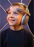 Smiling young boy wearing headphones with a brainwave headset in a high-tech room.