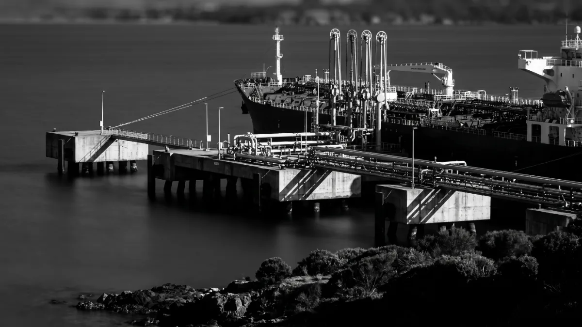Pipelines and loading arms reaching from mooring dolphins to a tanker on a sheltered bay.