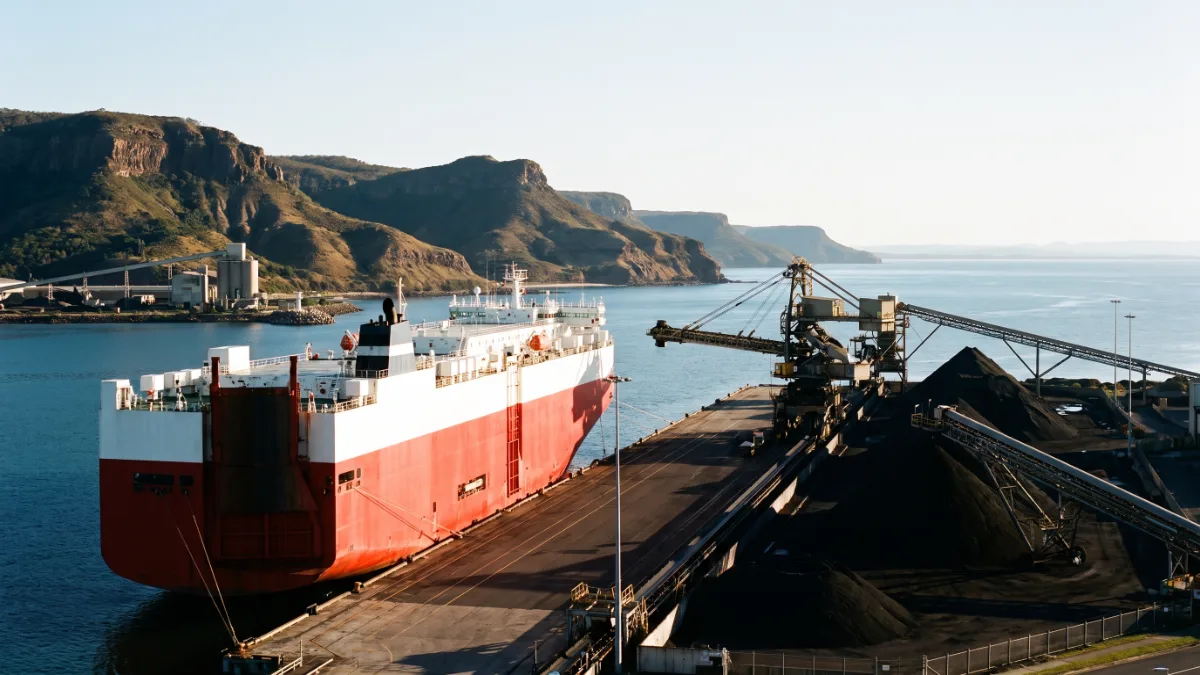 A steelworks harbour with a roll on roll off ship at the vehicle wharf and hills behind.
