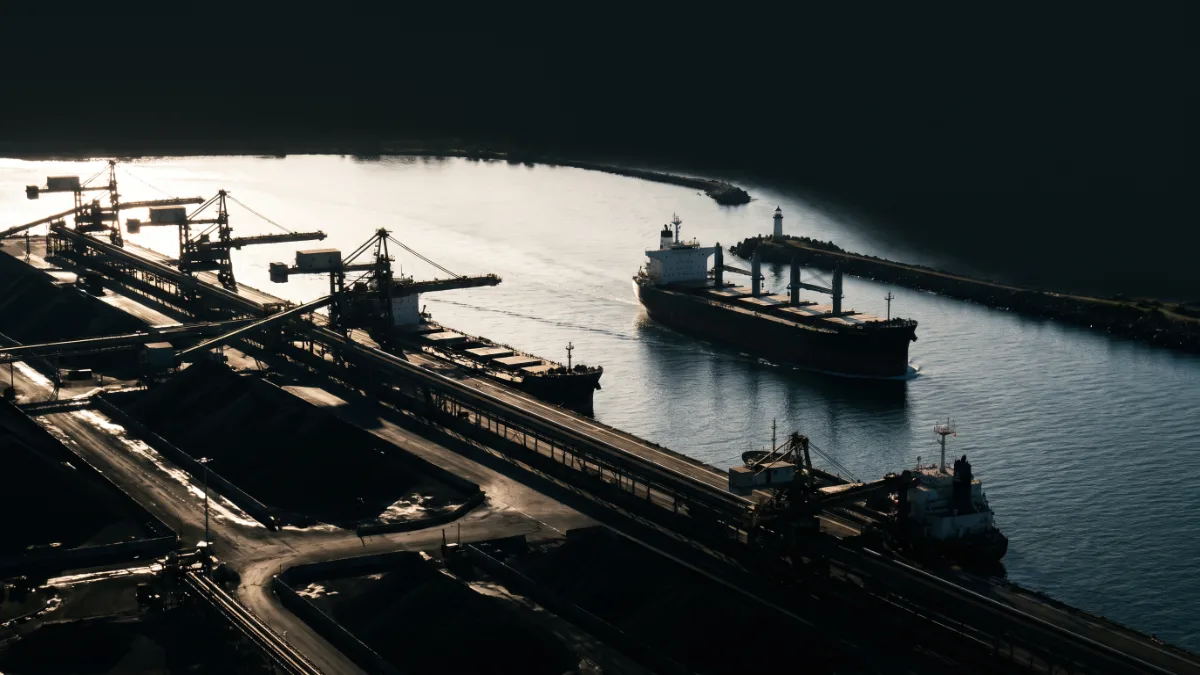 Ship loaders line the wharves as a bulk carrier moves through a river harbour entrance.