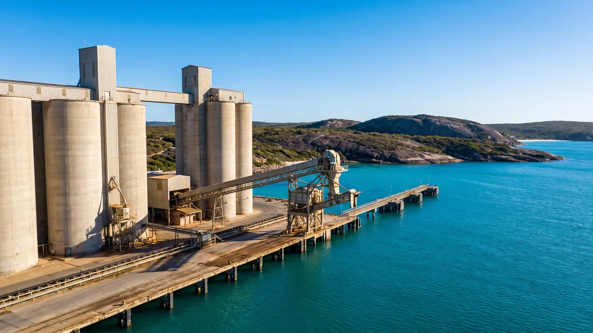 Grain silos and a conveyor loader on a wharf, with granite headlands and turquoise Southern Ocean water behind.