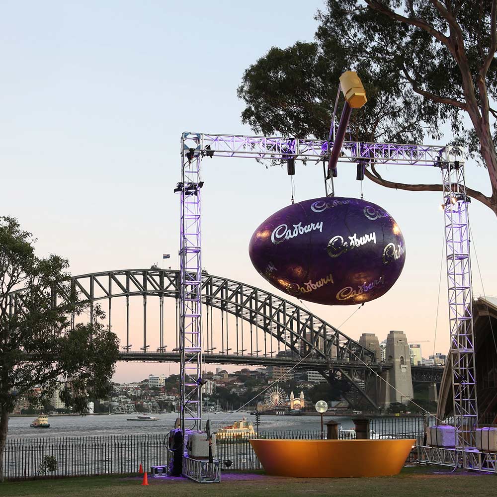 huge cadbury easter egg hanging from a metal scaffold with the sydney harbour bridge in the background