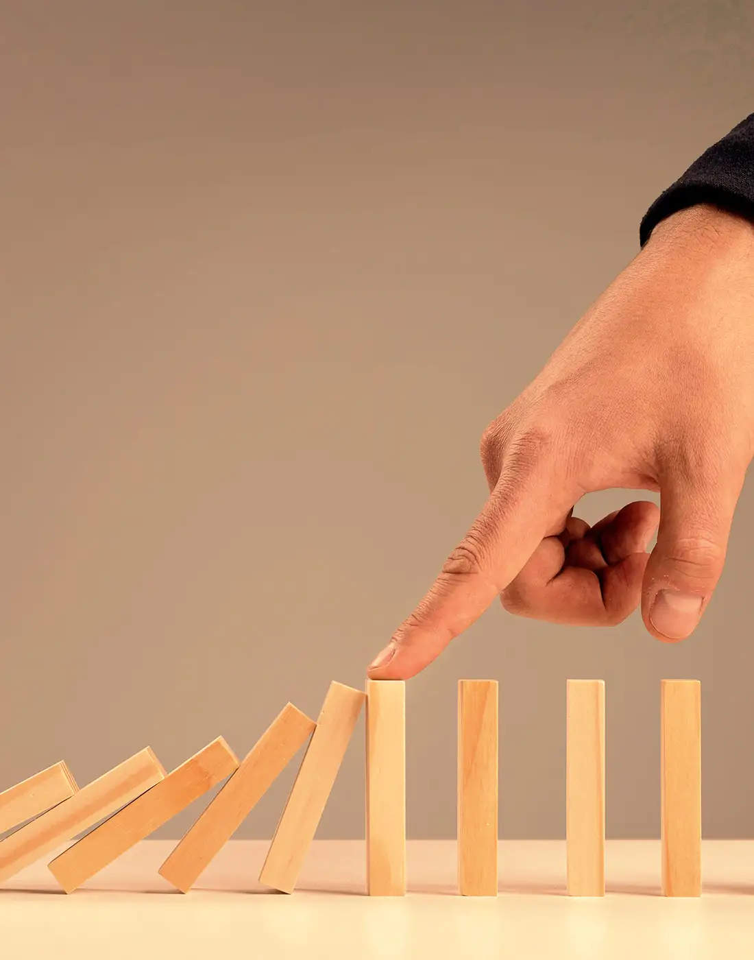 Hand stopping wooden blocks from falling, symbolising effective liquidity and risk management to protect investments.