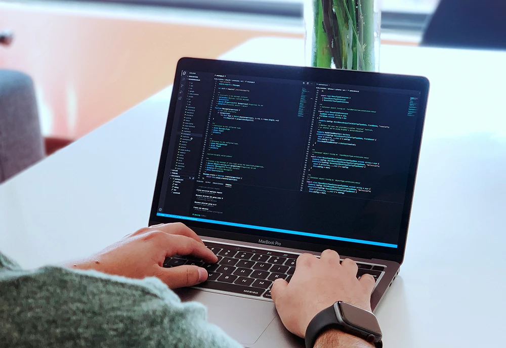 Photot taken from behind of a man, coding on his laptop.