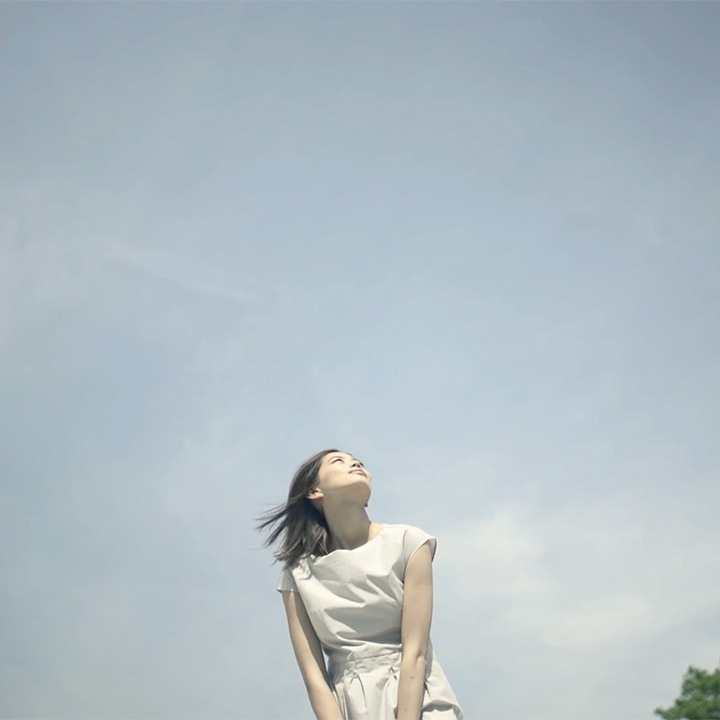 Young woman in a light dress looking up against a clear blue sky.