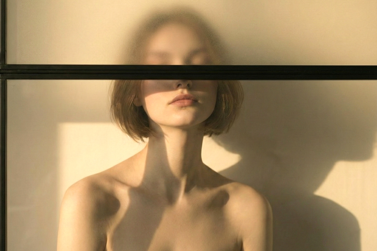 Woman with short hair standing behind frosted glass, her eyes obscured by a horizontal line.