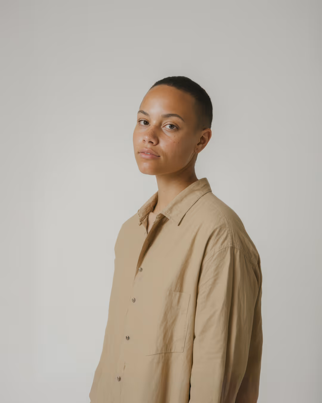 Portrait of a person with short hair wearing a beige button-up shirt against a plain light background.