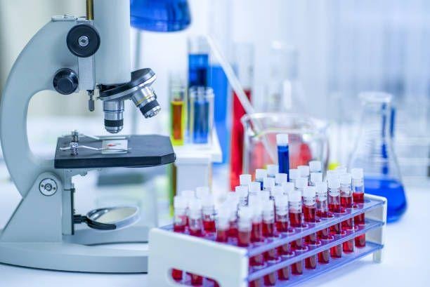 This may contain: a microscope filled with red liquid in front of some test tubes and flasks