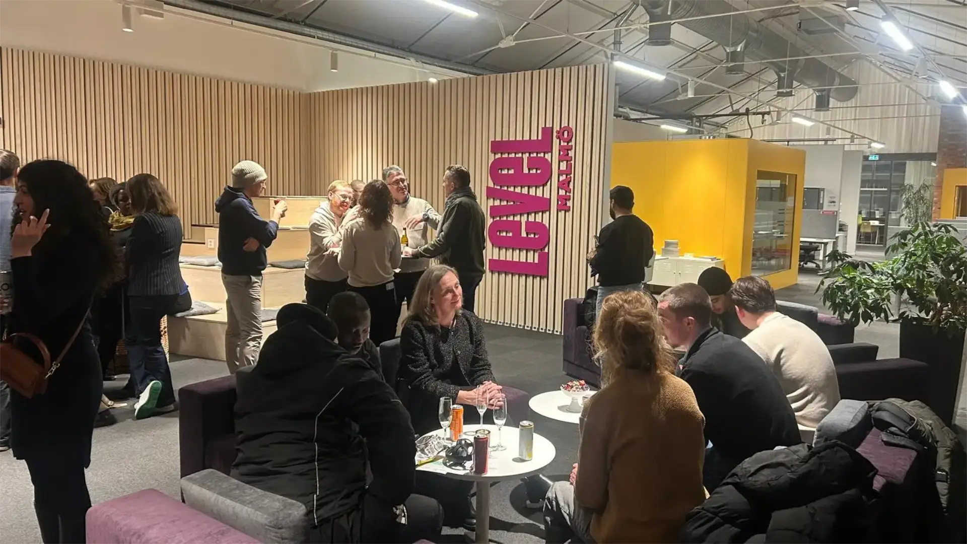 Människor umgås och samtalar i en modern lounge med texten Level Malmö på väggen.
