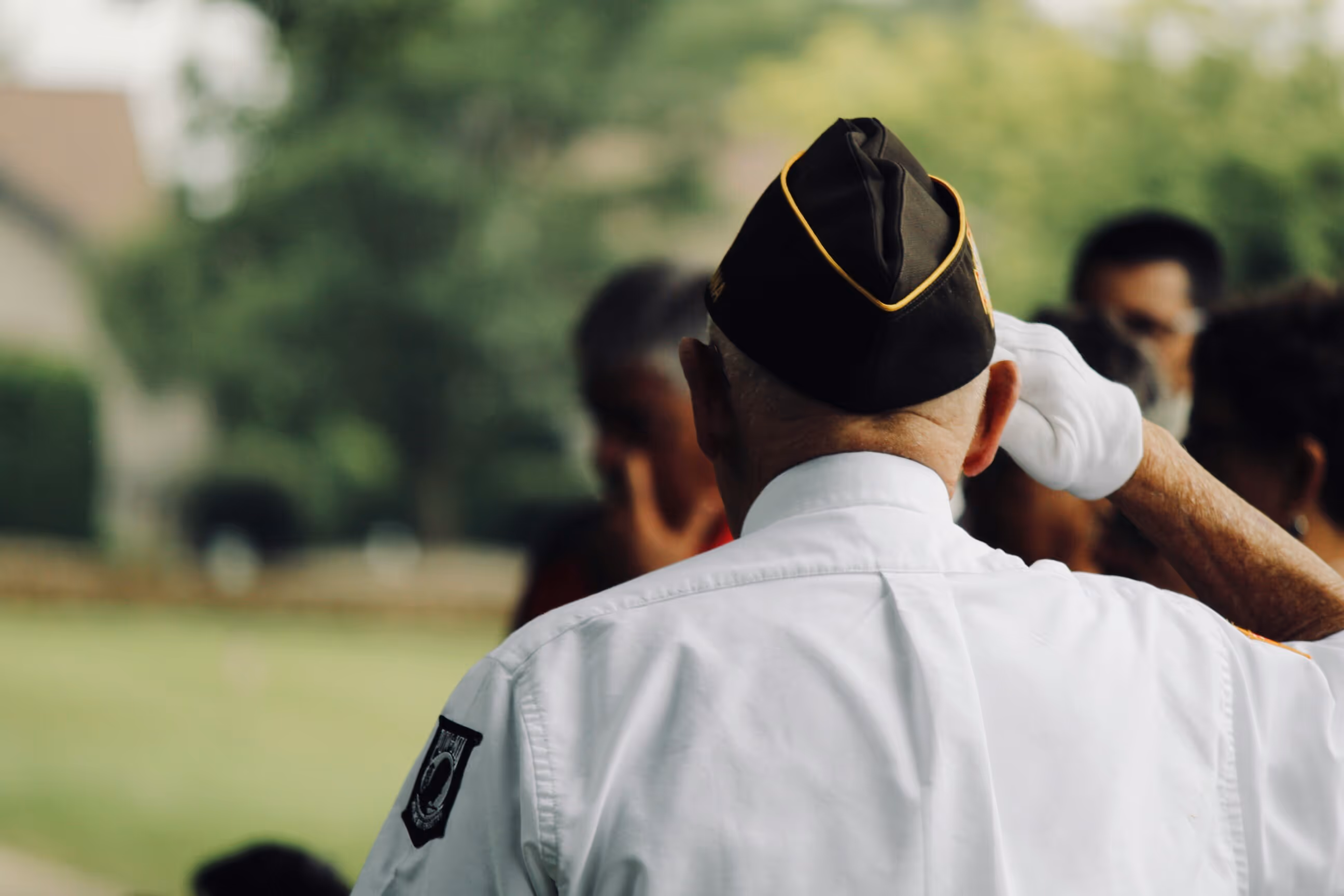 A veteran salutes during a memorial event in a serene outdoor setting.