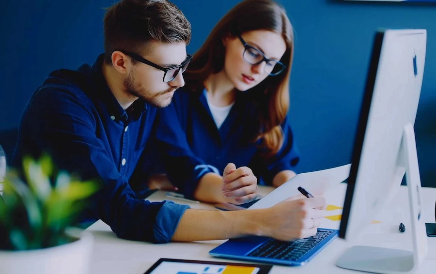 Two coworkers analyzing a risk impact matrix on a computer screen in an office setting.